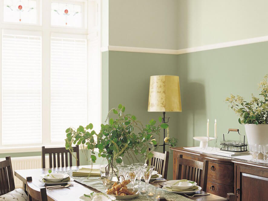 Traditional dining setting with a pop of green on the walls yellow lamp plants and wooden table